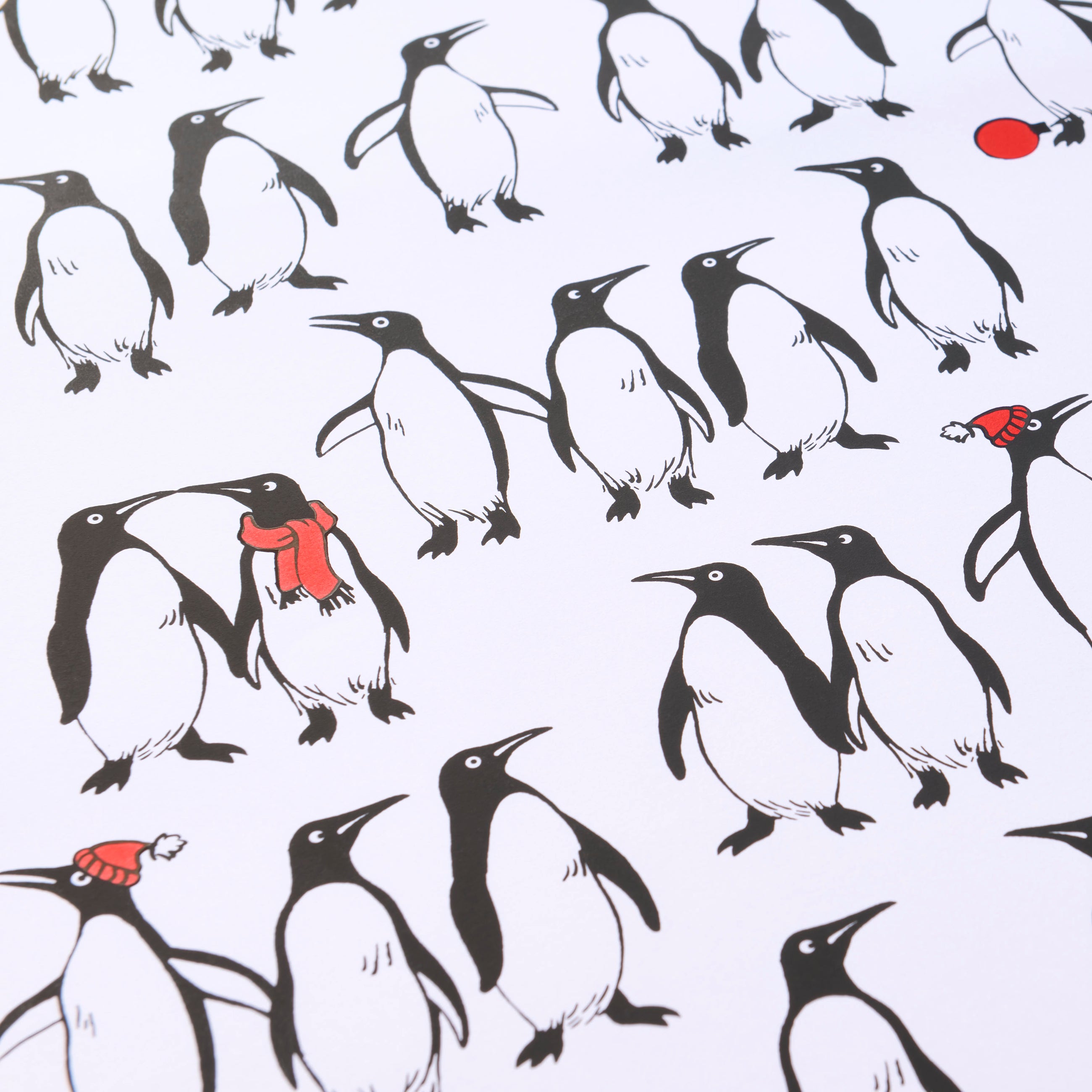 Wrapping paper with a playful pattern of black-and-white penguins on a crisp white background, with a few penguins accented by bright red scarves or hats for a festive touch.