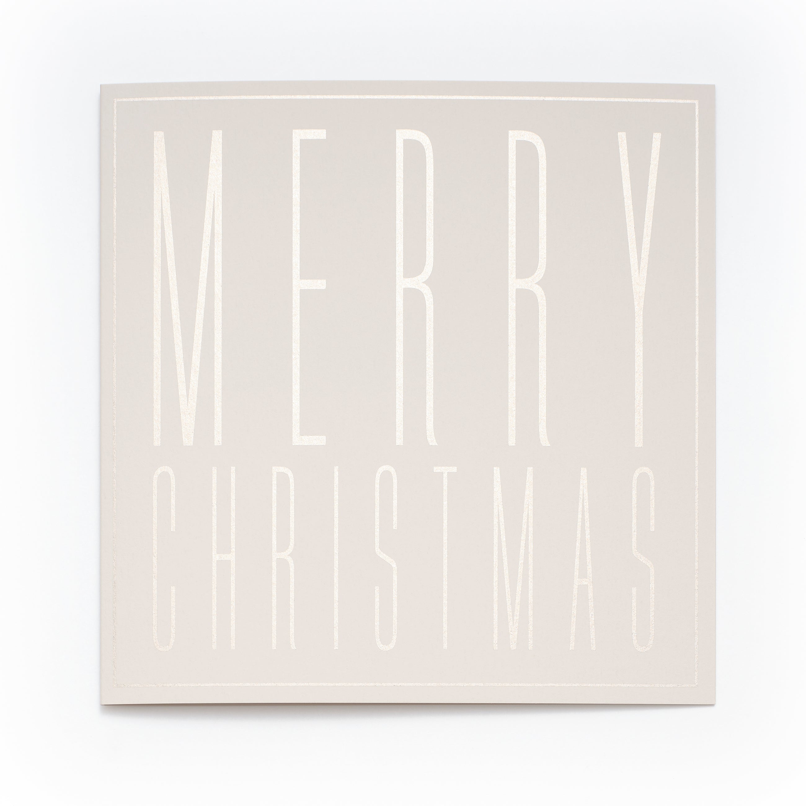 A square cream-colored Christmas card with embossed tall block letters spelling "MERRY CHRISTMAS".