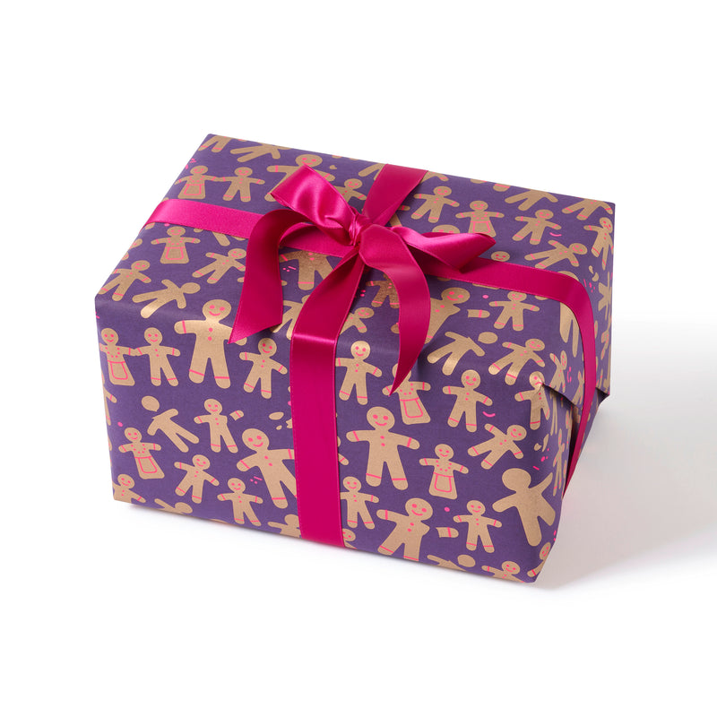 A gift wrapped in festive paper decorated with golden gingerbread men and women on a deep purple background, finished with a vibrant pink satin ribbon.
