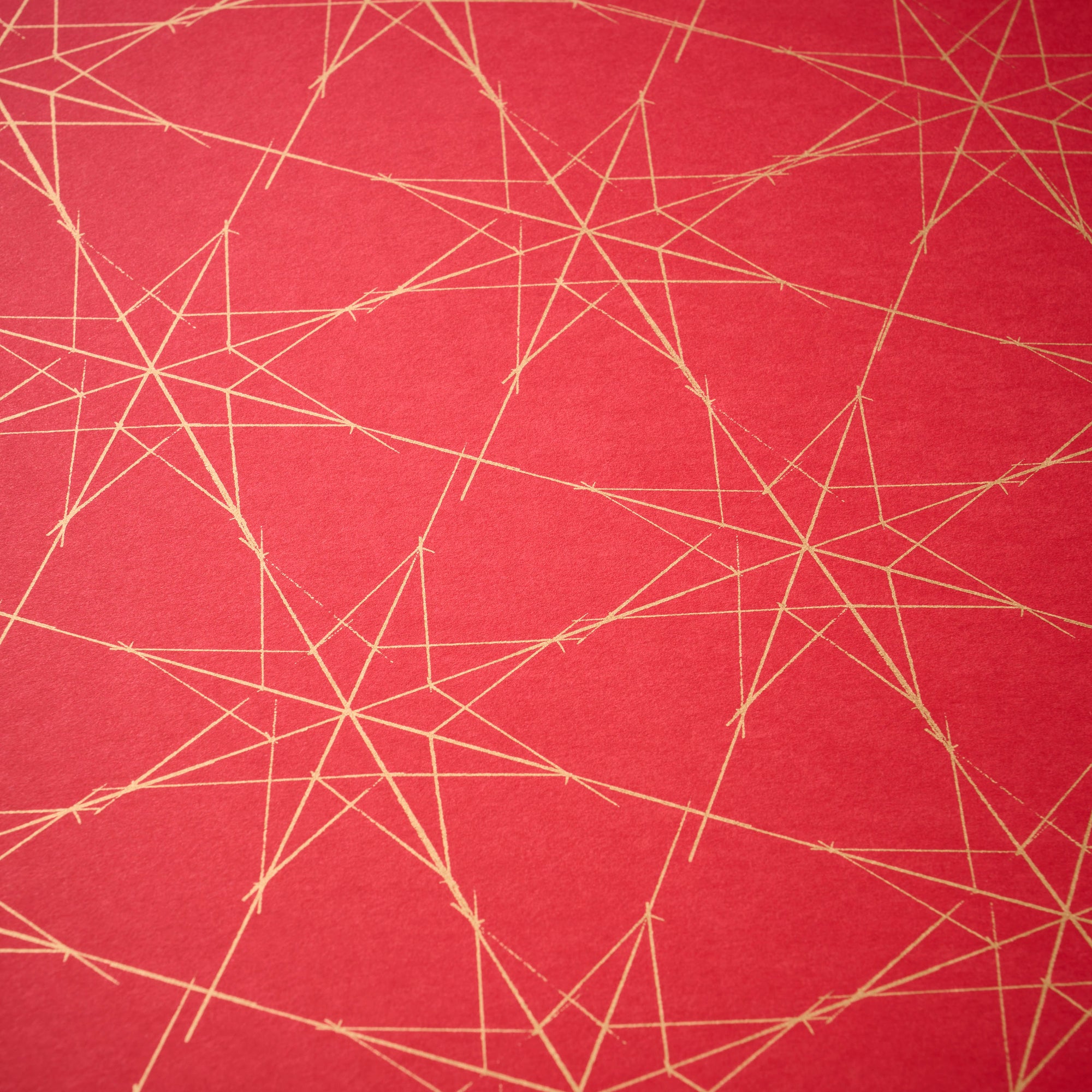 Wrapping paper with a festive pattern of fine golden star outlines scattered across a deep red background.