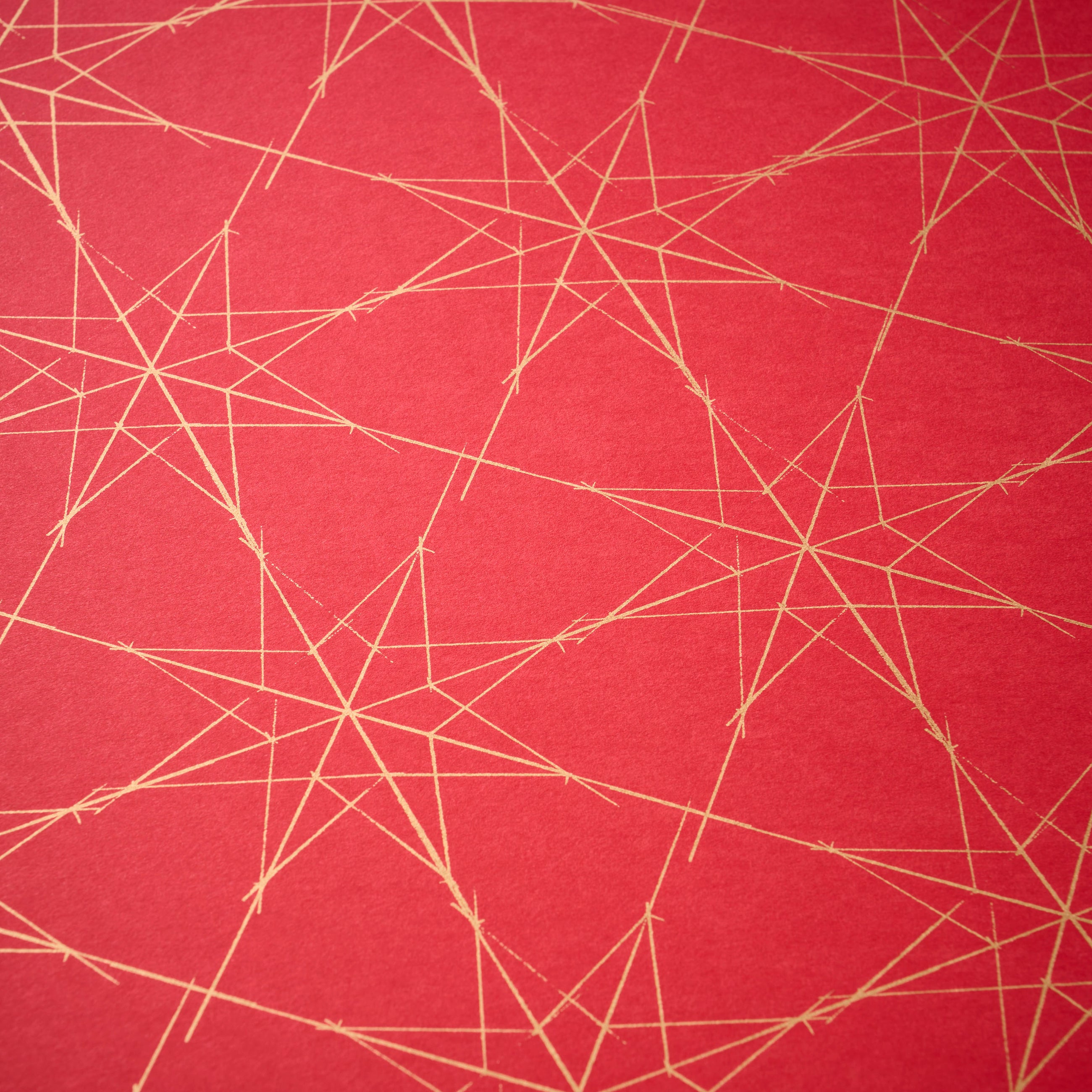 Wrapping paper with a festive pattern of fine golden star outlines scattered across a deep red background.