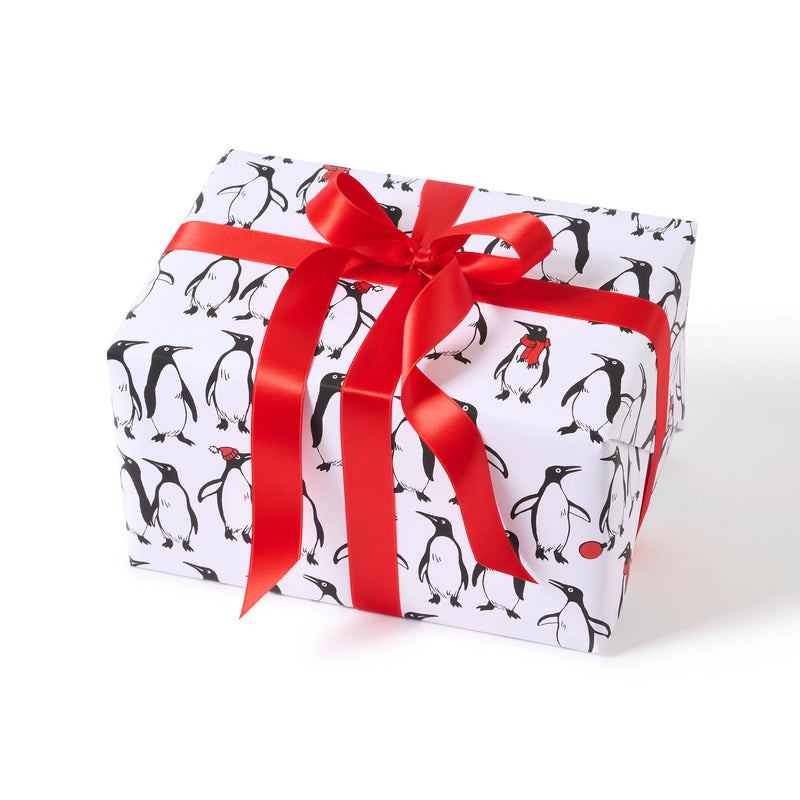 A gift wrapped in festive penguin-patterned paper, showcasing black-and-white penguins on a white background, tied neatly with a bold red satin ribbon for a bright holiday finish.