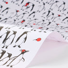 Wrapping paper featuring a lively crowd of black-and-white penguins against a white background, with scattered red holiday accents such as ornaments and hats adding a cheerful pop of color.