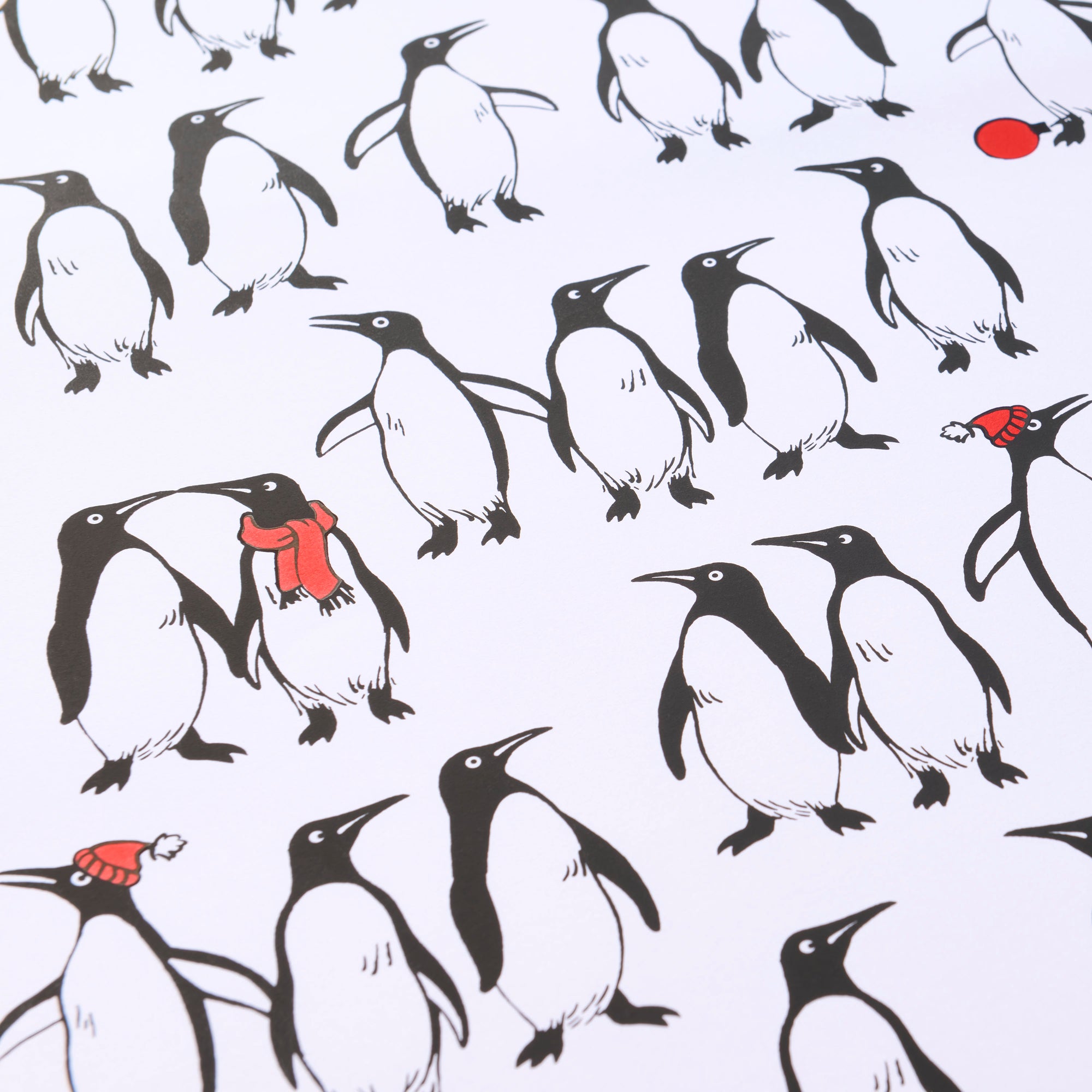 Wrapping paper with a playful pattern of black-and-white penguins on a crisp white background, with a few penguins accented by bright red scarves or hats for a festive touch.