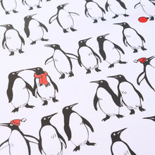 Wrapping paper with a playful pattern of black-and-white penguins on a crisp white background, with a few penguins accented by bright red scarves or hats for a festive touch.