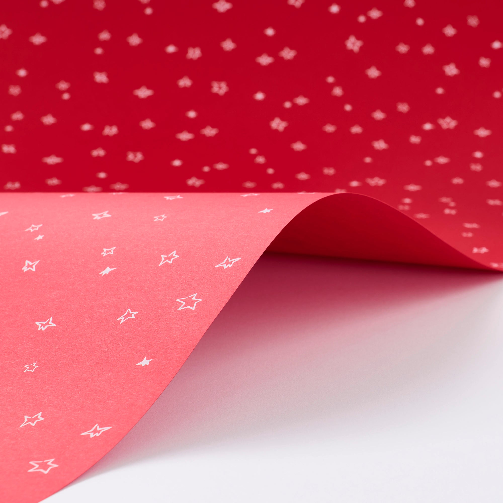 Wrapping paper with a festive pattern of tiny white sketchy stars scattered across a vivid red background.