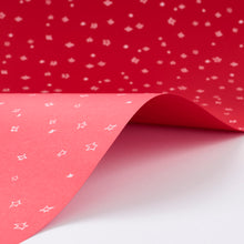Wrapping paper with a festive pattern of tiny white sketchy stars scattered across a vivid red background.