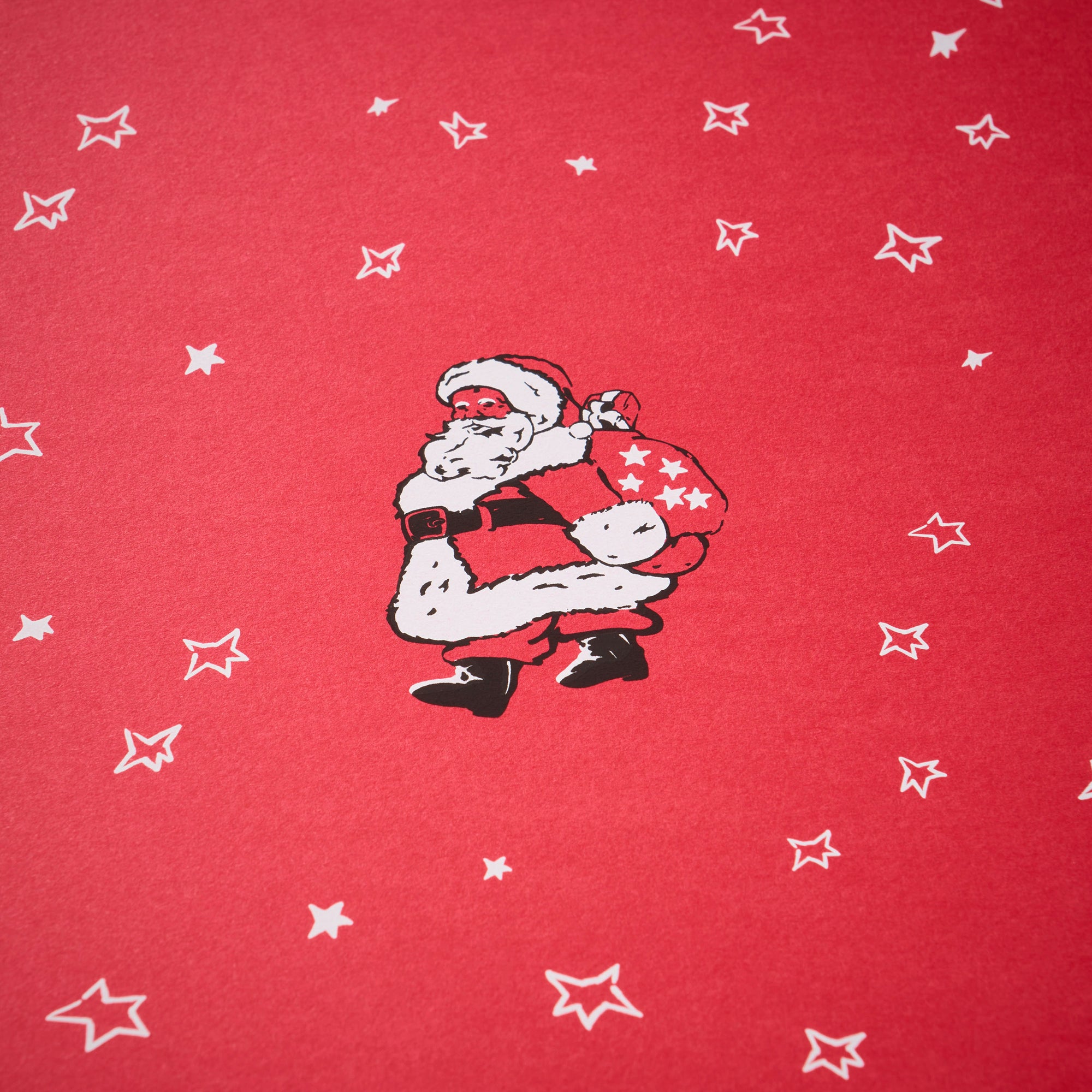 Wrapping paper with a festive pattern of a vintage-style Santa carrying a star-covered sack, surrounded by scattered white hand-drawn stars on a bright red background.