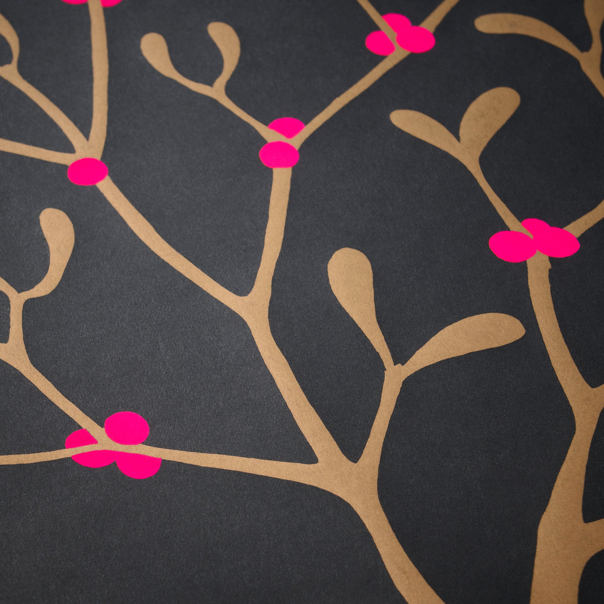 Wrapping paper with a festive pattern of golden mistletoe branches scattered across a deep charcoal background, accented by bright pink berries.
