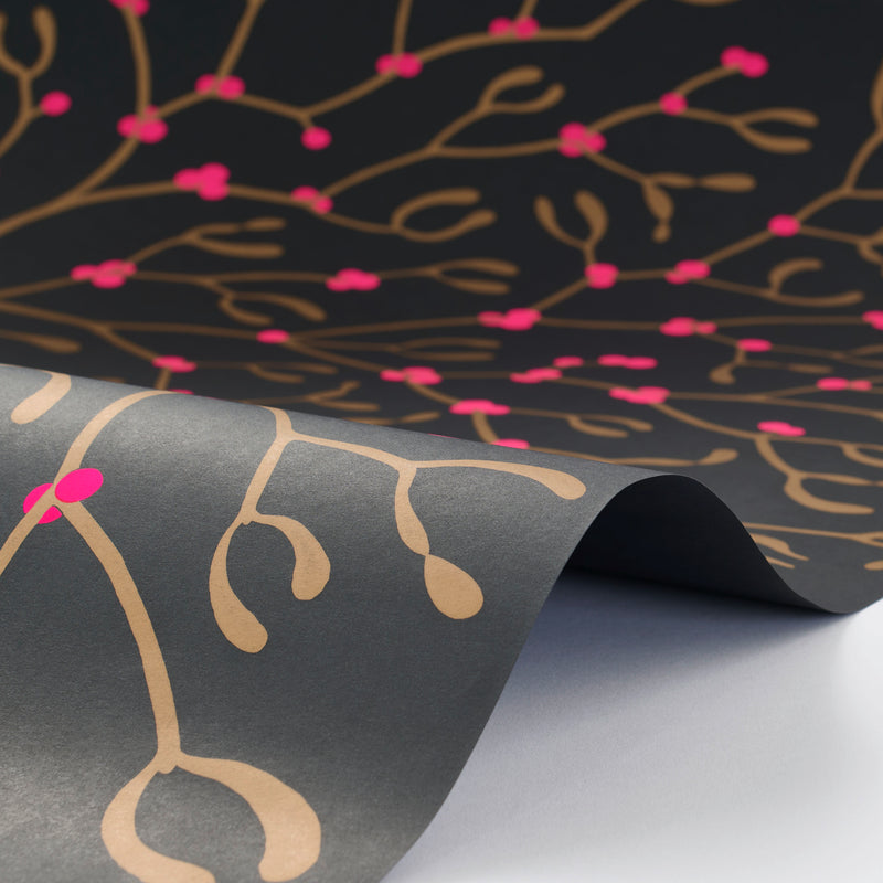 Wrapping paper with a festive pattern of golden mistletoe branches on a deep charcoal background, highlighted by vivid pink berries and shown in a softly curved sheet.