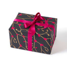A gift wrapped in festive paper featuring golden mistletoe branches on a deep charcoal background, tied with a vibrant pink satin ribbon.