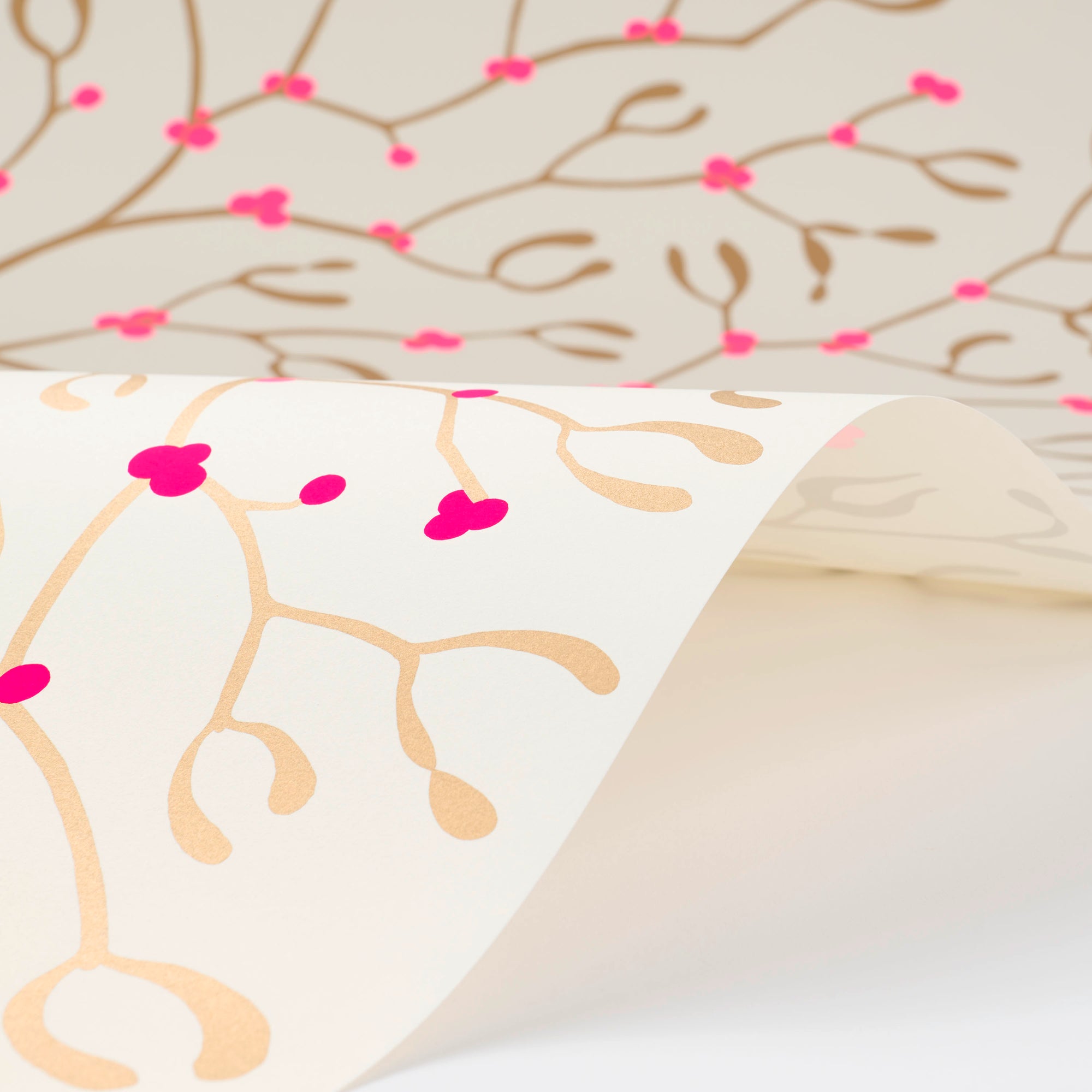 Wrapping paper with a festive pattern of golden mistletoe branches and vivid pink berries, shown gently curled to display the repeating design on a cream-white background.