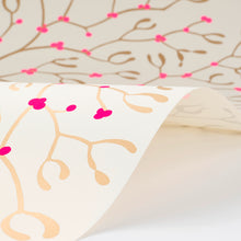 Wrapping paper with a festive pattern of golden mistletoe branches and vivid pink berries, shown gently curled to display the repeating design on a cream-white background.