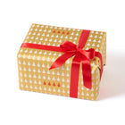 Wrapped gift in paper featuring a festive pattern of small white Christmas trees on a glowing gold background, with a bold red ribbon and a row of vivid red trees adding a cheerful contrast.