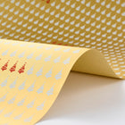 Wrapping paper with a festive pattern of white Christmas trees arranged in neat rows on a warm golden sheet, featuring a subtle highlight of red trees repeating through the design.