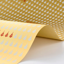 Wrapping paper with a festive pattern of white Christmas trees arranged in neat rows on a warm golden sheet, featuring a subtle highlight of red trees repeating through the design.