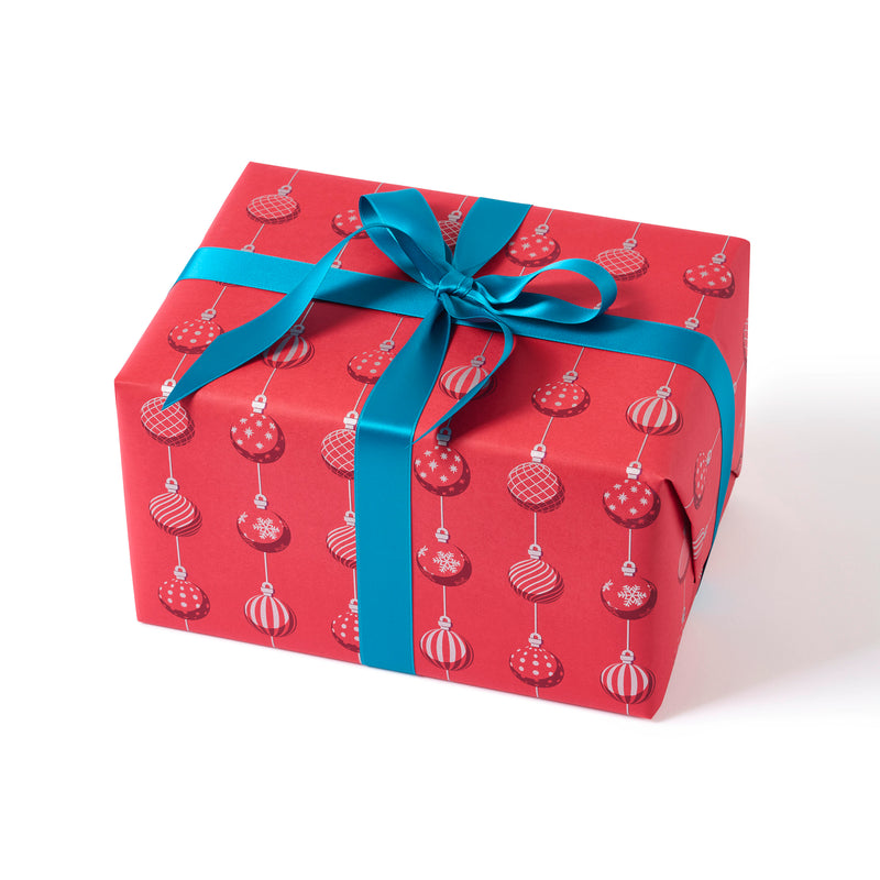 A gift wrapped in festive red paper patterned with red and white Christmas baubles in vertical rows, finished with a bright blue satin ribbon tied in a bow.