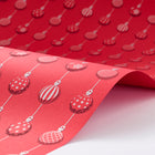 Wrapping paper with a festive pattern of varied red and white Christmas baubles in neat vertical rows, shown in a gently curved sheet to highlight texture and print.