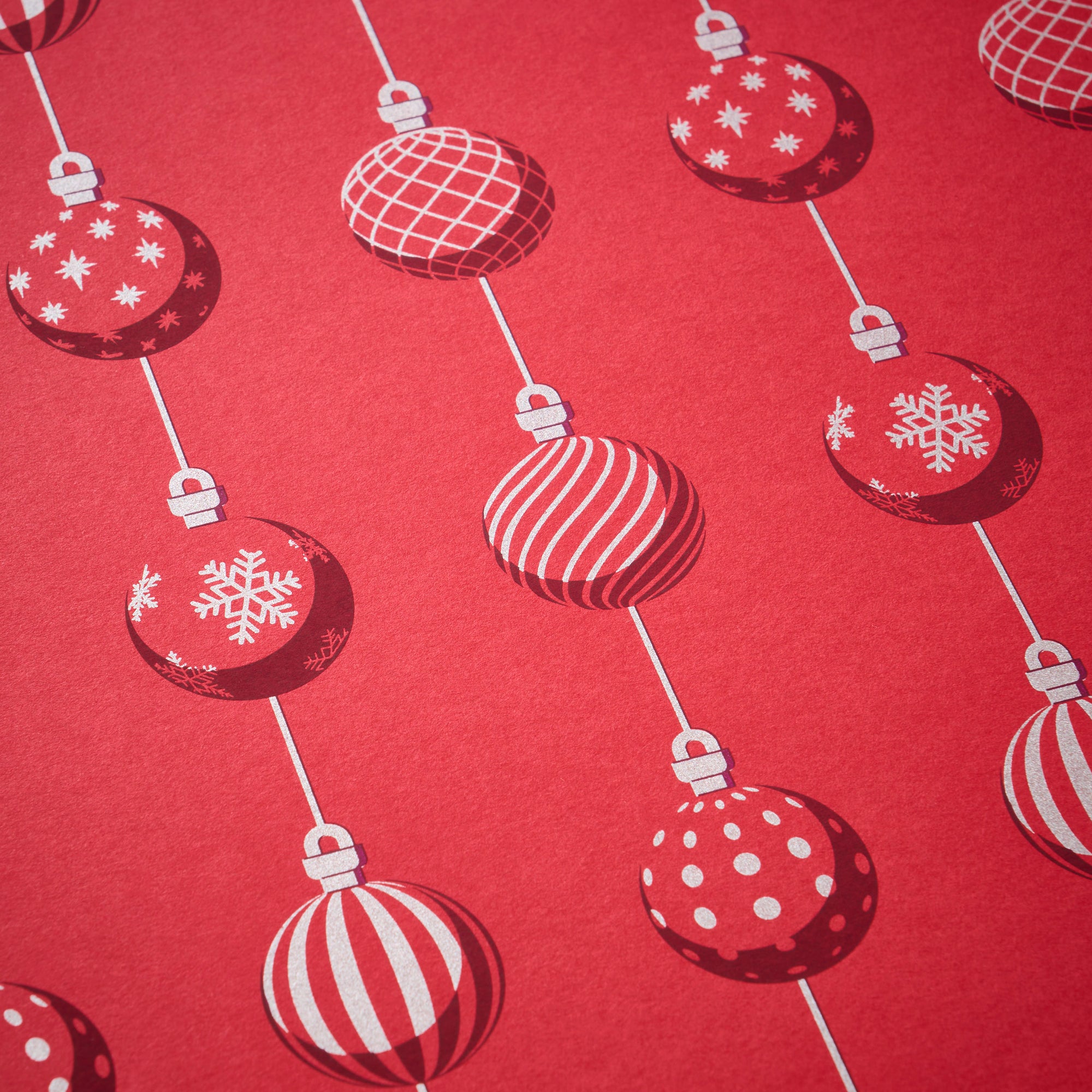 Wrapping paper with a festive pattern of red Christmas baubles decorated in white snowflakes, stripes, grids, and polka dots, arranged in vertical lines against a bright red background.