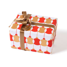 A gift wrapped in festive paper featuring red and gold baubles on a white background, finished with a smooth bronze satin ribbon.