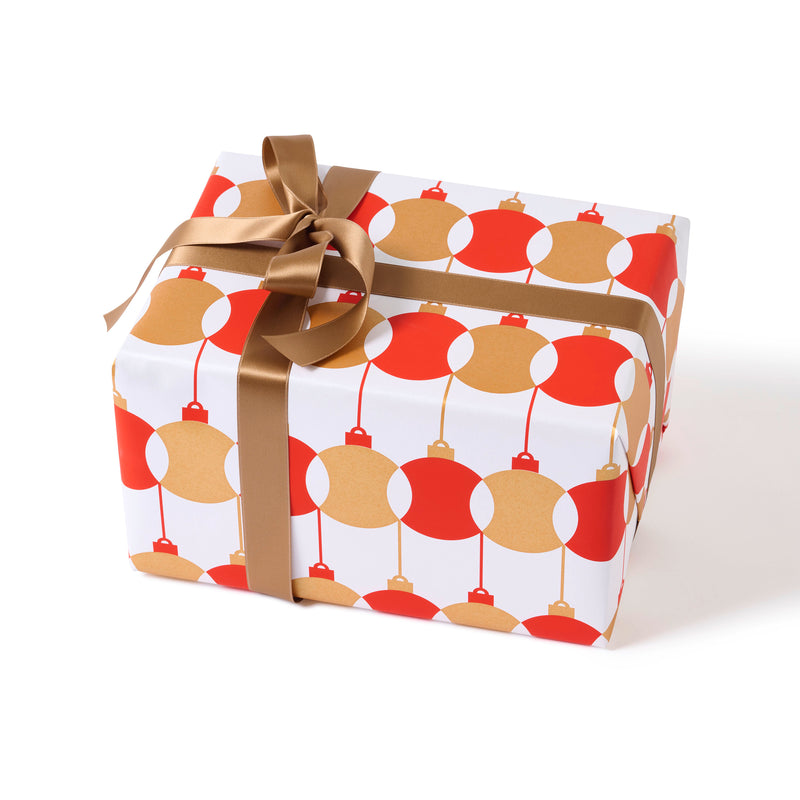 A gift wrapped in festive paper featuring red and gold baubles on a white background, finished with a smooth bronze satin ribbon.