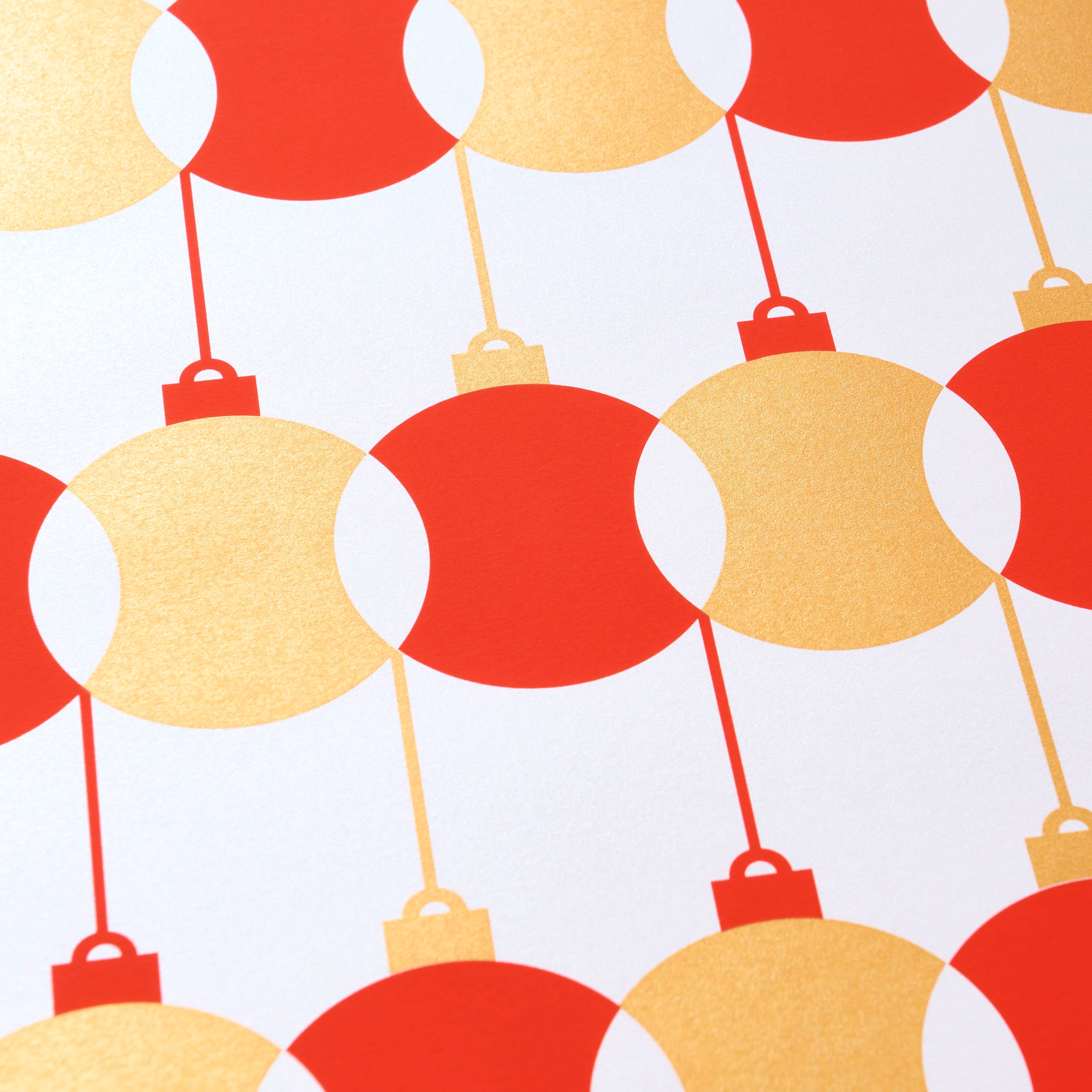 Wrapping paper with a festive pattern of red and gold baubles arranged in a bold geometric row across a bright white background.