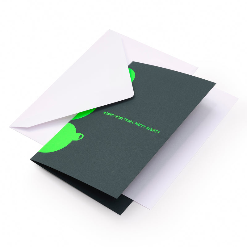 A dark green holiday card with bright neon green ornament shapes along the edges and the text "MERRY EVERYTHING. HAPPY ALWAYS" in matching neon green at the center, shown with a plain white envelope.