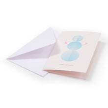 A light pink holiday card with a minimalist blue snowman design made of three patterned circles, simple pink stick arms, and the text "HAPPY HOLIDAYS" in pink at the bottom, shown with a plain white envelope.