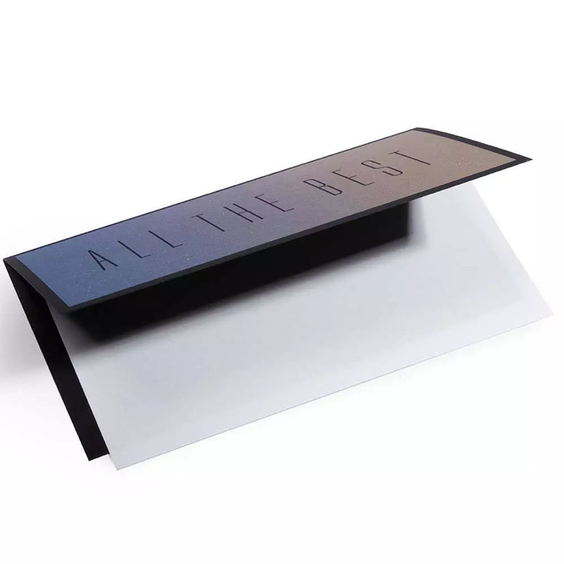 A folded greeting card shown at an angle with a subtle gradient from blue to warm yellow, featuring the words “ALL THE BEST” in thin, understated typography on the front.