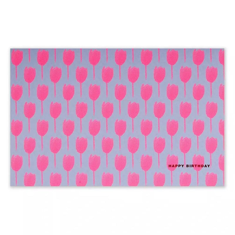 A rectangular greeting card with a lilac background, covered in a repeating pattern of bright pink tulip silhouettes, with “HAPPY BIRTHDAY” printed in small text in the corner.