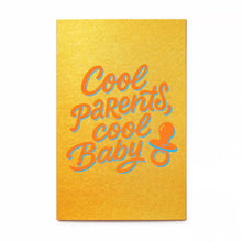 A vibrant greeting card with a warm golden-yellow background, featuring playful script lettering in bright orange with a soft blue shadow reading “Cool parents, cool baby,” alongside a small pacifier icon.
