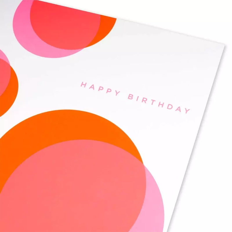 A close-up of a white greeting card with layered orange and pink circular shapes, with “HAPPY BIRTHDAY” printed in a light, minimalist font.