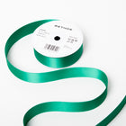 A spool of satin ribbon in emerald green, partially unrolled, with a white label on top reading “BETHGE” and product details including width, length, and material.