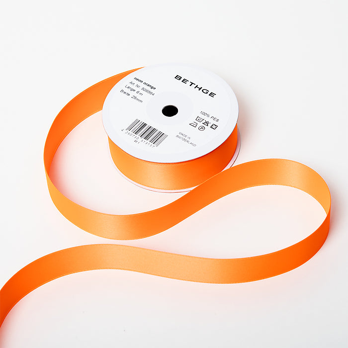 A spool of satin ribbon in neon orange, partially unrolled, with a white label on top reading “BETHGE” and product details including width, length, and material.