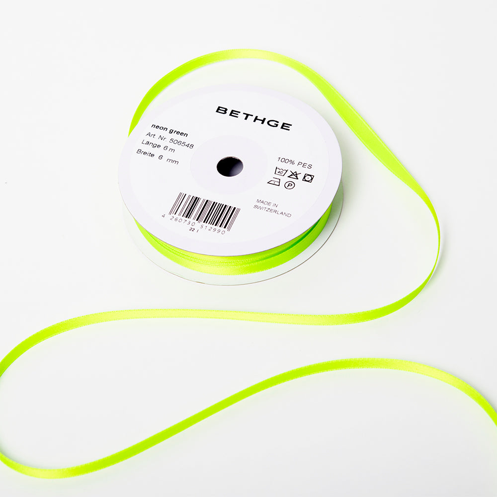 A spool of satin ribbon in neon green, narrow in width, partially unrolled, with a white label on top reading “BETHGE” and product details including width, length, and material.