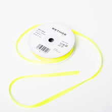 A spool of satin ribbon in neon yellow, narrow in width, partially unrolled, with a white label on top reading “BETHGE” and product details including width, length, and material.