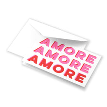 Greeting card partially pulled from a white envelope, featuring the word “AMORE” repeated in large pink and red letters, creating a playful, modern love-themed design.