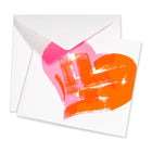 Greeting card with a bold neon pink and orange painted heart on a white background, shown partially open with a white envelope behind it, emphasizing the modern, artistic brushstroke design.