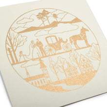 A close-up of a circular gold-foil illustration depicting a bride and groom with a horse-drawn carriage, trees, and a village.