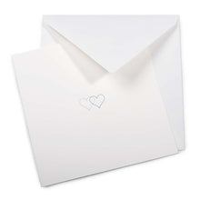 A soft ivory greeting card partly pulled from a matching envelope, featuring two fine-line hearts in blue and lilac printed at the center.