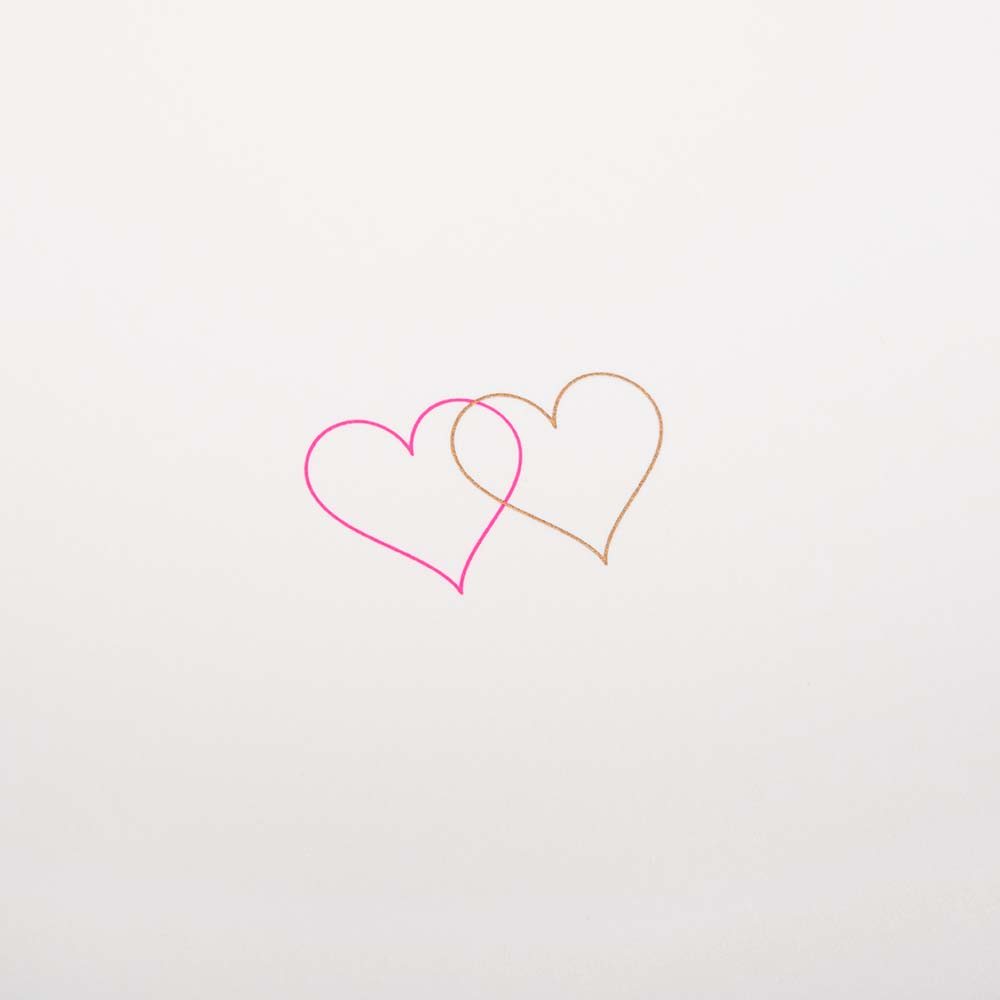 Close up of an ivory greeting card with two small overlapping hearts in pink and gold set against a clean, minimal background.