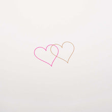 Close up of an ivory greeting card with two small overlapping hearts in pink and gold set against a clean, minimal background.