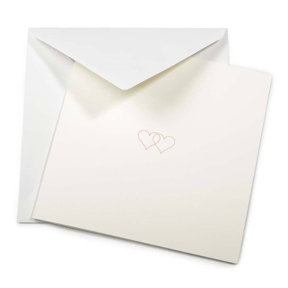 A soft ivory greeting card partly pulled from a matching envelope, featuring two fine-line hearts in pink and gold printed at the center.