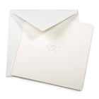 A soft ivory greeting card partly pulled from a matching envelope, featuring two fine-line hearts in pink and gold printed at the center.