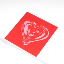 Greeting card with a minimalist design, featuring a painterly light-pink heart printed on a bold red square background, shown at a slight angle against a clean white surface.