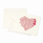 Greeting card with an elegant, minimalist design, featuring a textured heart made of overlapping pink feather motifs on warm off-white paper, displayed with a matching envelope beside it.