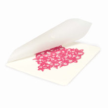 Greeting card with a delicate, handmade look, featuring a heart shape formed from layered pink feather-like patterns on soft cream paper, shown slightly open with a translucent envelope above.