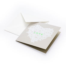 Greeting card with a refined, minimalist design, featuring a soft beige background and a heart formed from delicate white feather-like textures, with the word “LOVE” in subtle neon green at the center, shown partially open with a matching white envelope behind it.