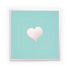 Greeting card with a minimalist design, featuring a soft blush-pink heart centered on a mint-green background framed by a subtle pale-pink border, presented straight-on with a calm, airy studio feel.