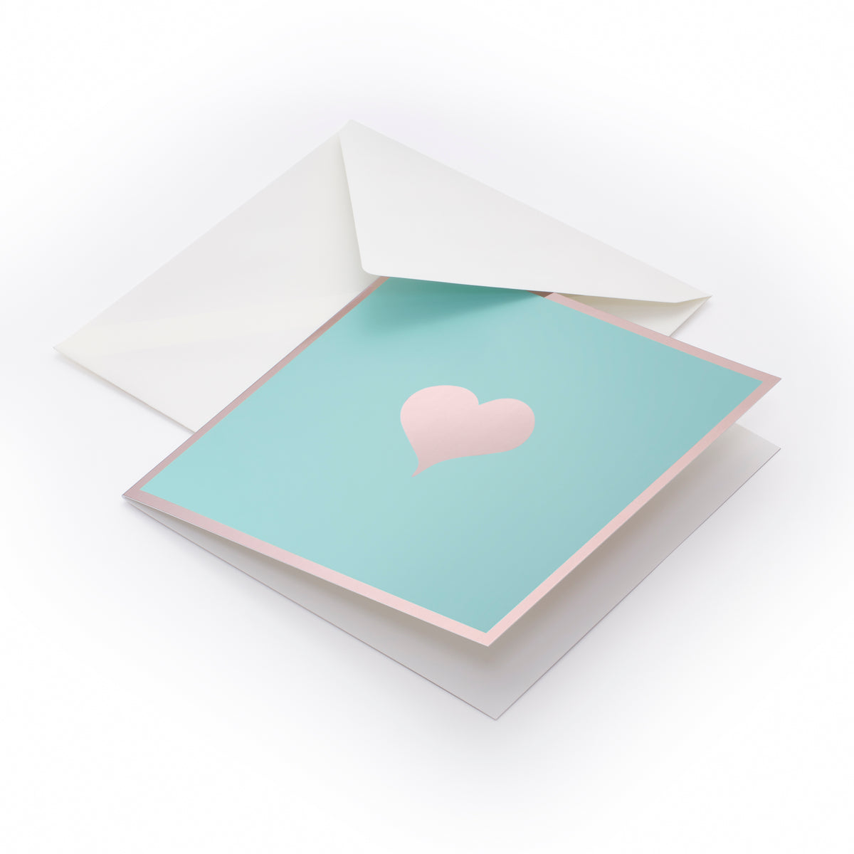 Greeting card with a minimalist design, featuring a soft blush-pink heart centered on a mint-green card bordered in pale pink, shown partially tucked into a white envelope at a gentle angle.